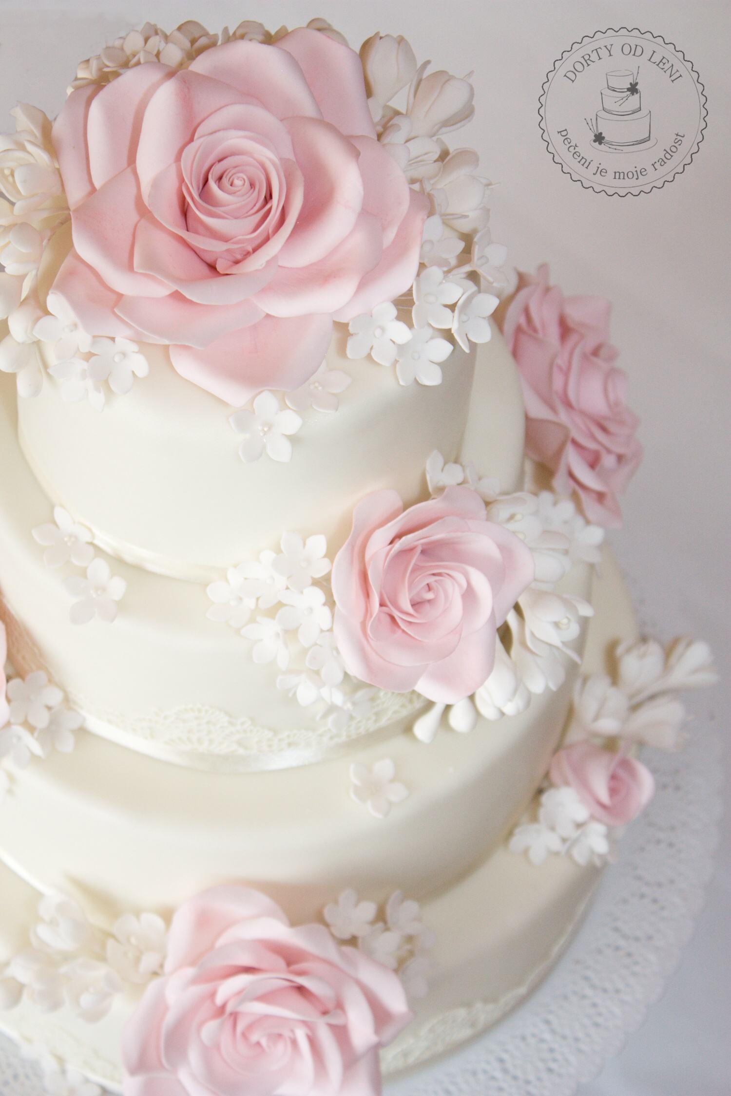 Svatební dort v krémové barvě s krajkou, růžemi a fréziemi.